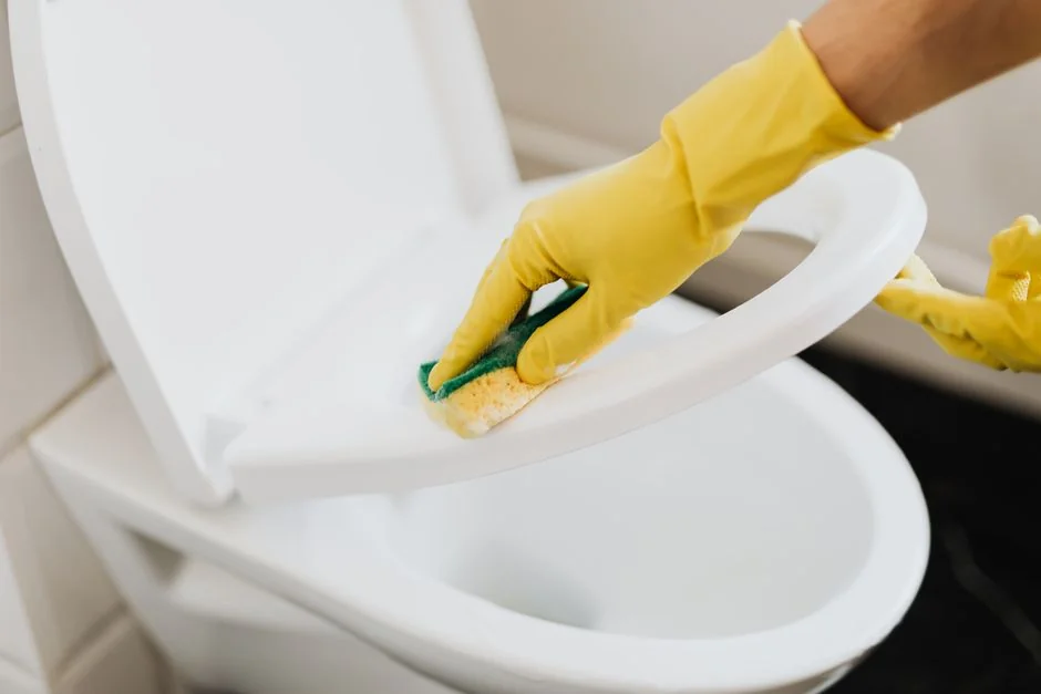 Vue prise d’en haut d’un(e) employé(e) d’entretien anonyme, en gants jaunes en caoutchouc, pulvérisant un nettoyant sur un robinet chromé dans une salle de bain